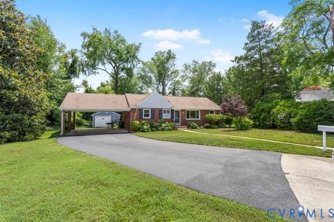 Brick facade home with a covered carport, expansive paved driveway, and mature landscaping