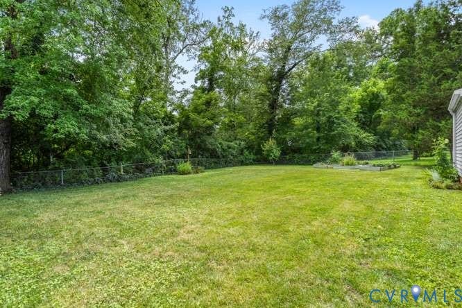 Expansive backyard featuring a lush lawn, mature trees providing natural screening, a chain-link fence, and a raised garden bed