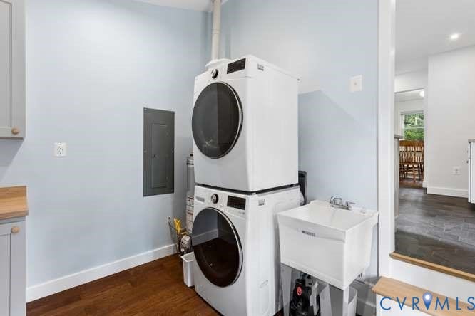 Dedicated laundry area featuring stacked front-load machines, a utility sink, wood-finish flooring, and light blue walls with white trim