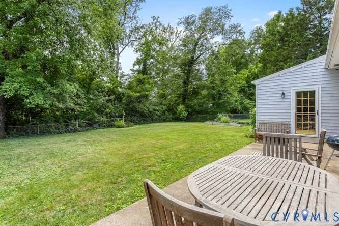 Expansive backyard featuring a large green lawn, mature perimeter trees, and a concrete patio