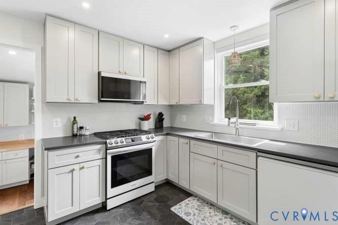 Contemporary kitchen featuring light gray cabinetry with gold-tone hardware, dark countertops, and a stainless steel appliance suite including a range and over-the-range microwave