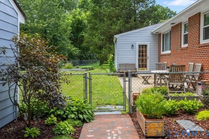 Brick patio with a glass-paned door and light blue siding, featuring a red brick walkway, chain link fence, and raised garden beds