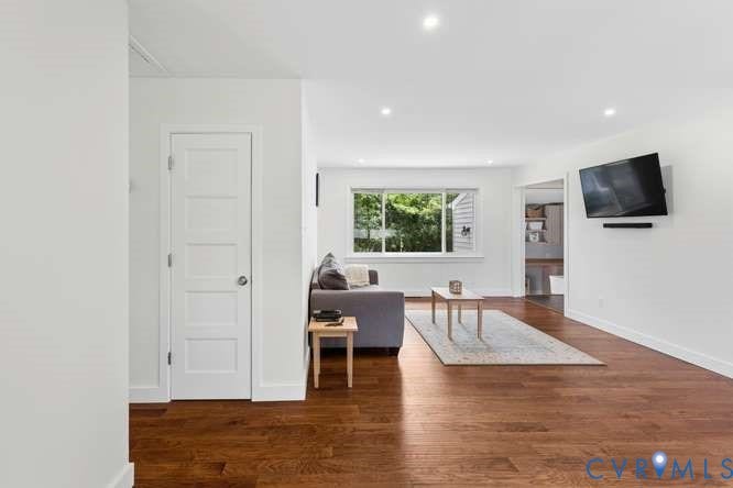 Expansive living area featuring rich wood-finish flooring, recessed lighting, white trim, and a large window