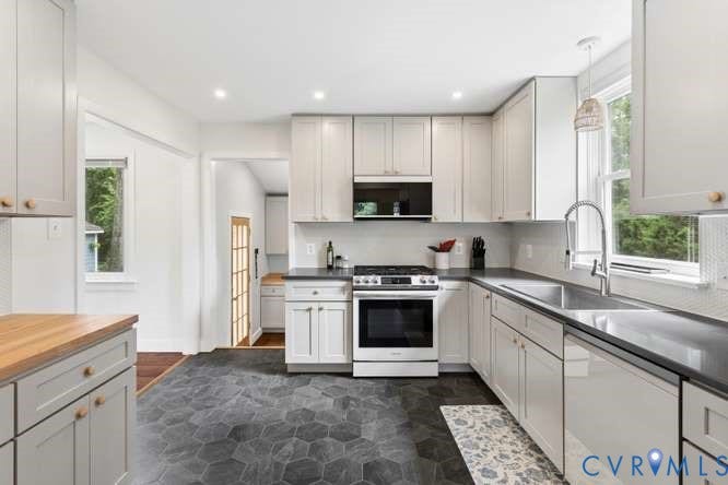 Contemporary kitchen featuring hexagonal floor tiling, light-toned cabinetry with wood knobs, dark countertops, and a full suite of stainless steel appliances