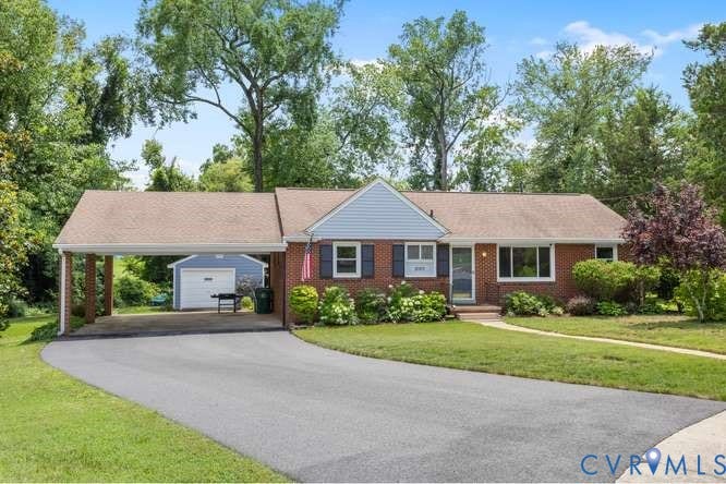 Brick facade residence featuring a covered carport, paved driveway, mature trees, and an additional detached garage structure