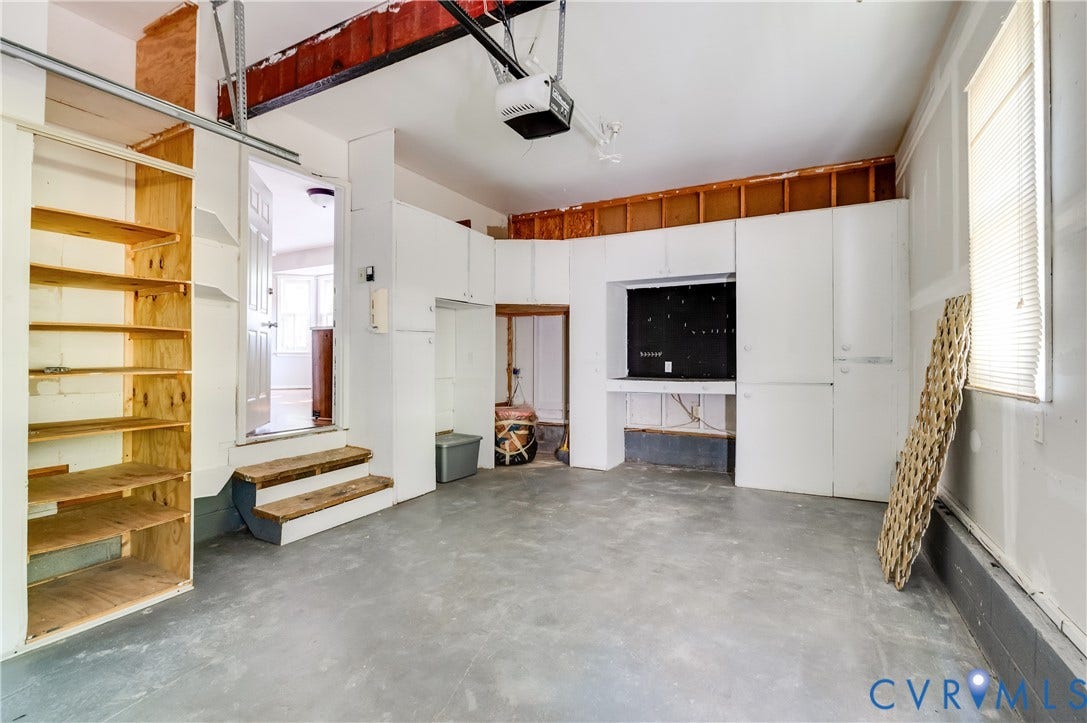 4419 Boones Bluff Way, Chesterfield, VA 23832 Spacious garage featuring concrete flooring, built-in shelving, white cabinetry, a dedicated workbench area, and natural light from a window with blinds