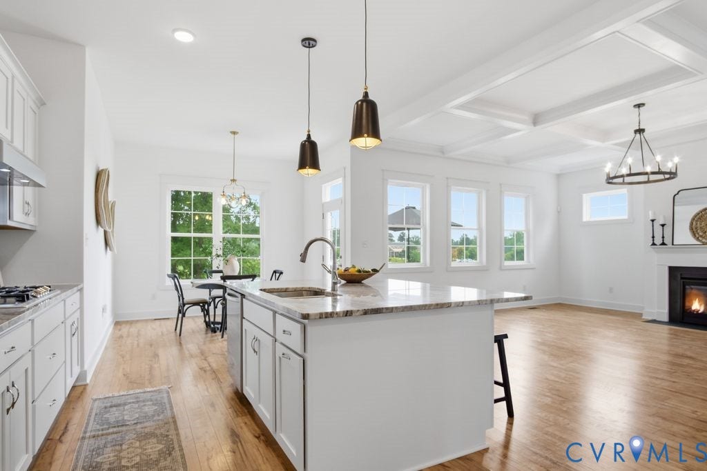 6991 Carden Park Drive, Carden Park, Moseley, VA 23120 Open-concept living area featuring a kitchen island with stone countertop, wood-finish flooring, white cabinetry, and a fireplace with a mantel