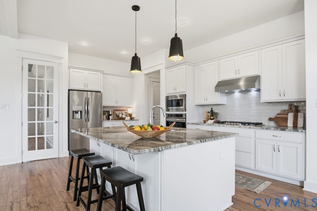 6991 Carden Park Drive, Carden Park, Moseley, VA 23120 Bright kitchen featuring a central island with a stone countertop, white cabinetry, stainless steel appliances, wood-finish flooring, and a French-paneled door