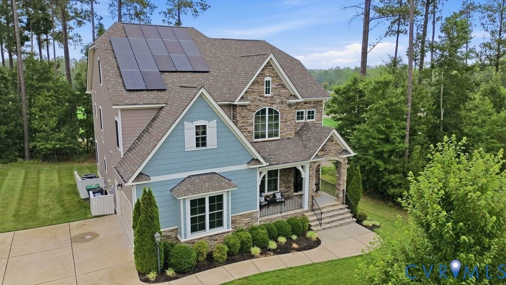 6991 Carden Park Drive, Carden Park, Moseley, VA 23120 Two-story residence featuring a stone and siding facade, covered front porch, integrated solar panels, a concrete driveway, and established landscaping