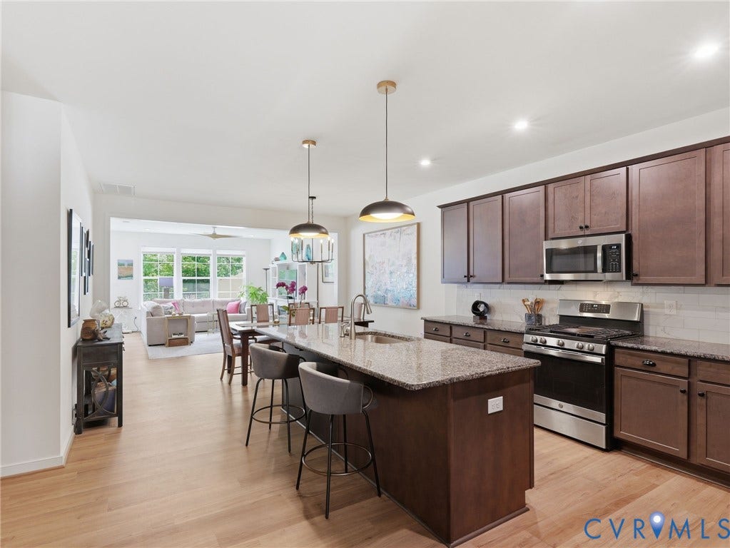 9237 Cerulean Place, Richmond, VA 23238 Stunning modern kitchen featuring granite countertops, stainless steel appliances, updated lighting. and beautiful wood laminate flooring, complete with a spacious pantry, custom contemporary wood cabinetry, and a luxurious island with built-in sink.