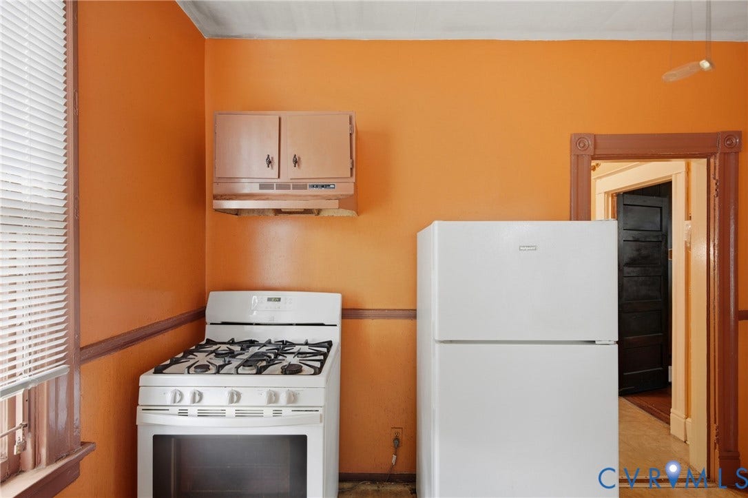 3110 North Avenue, Brookland Park, Richmond, VA 23222 Bright kitchen featuring vibrant orange walls, gas range with white enamel finish, white refrigerator with top-mount freezer, stainless steel wall-mounted cabinet, and wood-finish flooring throughout