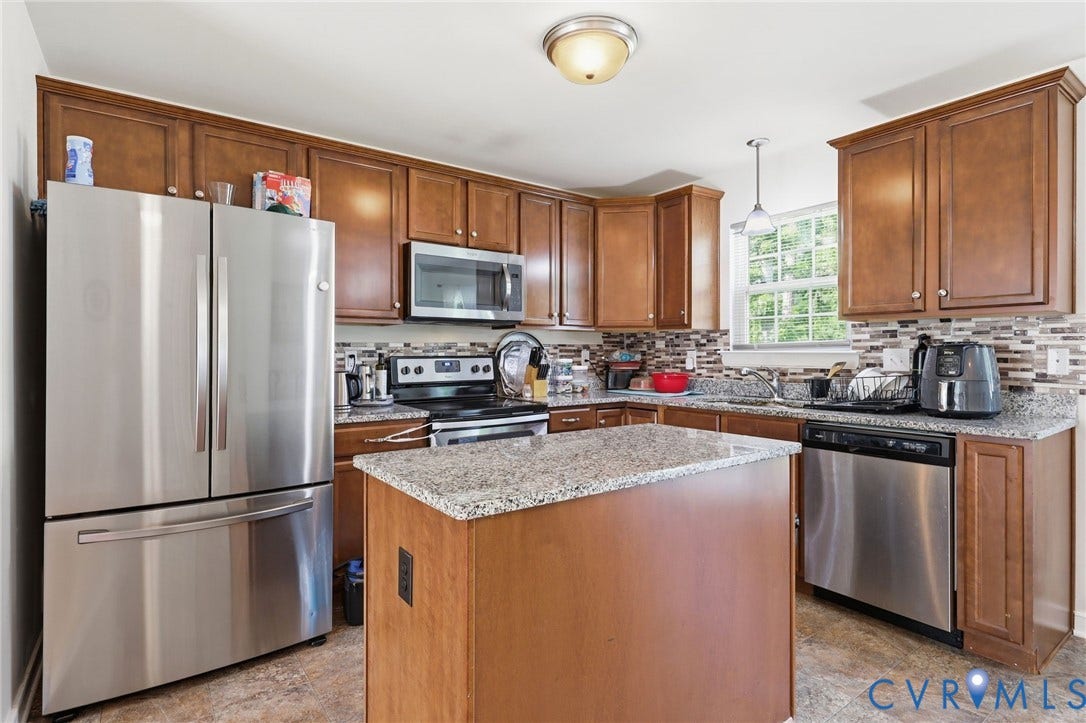10155 Virginia Road, Glen Allen, VA 23060 Kitchen featuring a central island with a granite-style countertop, stainless steel appliances, wood-finish cabinetry, and a mosaic tile backsplash