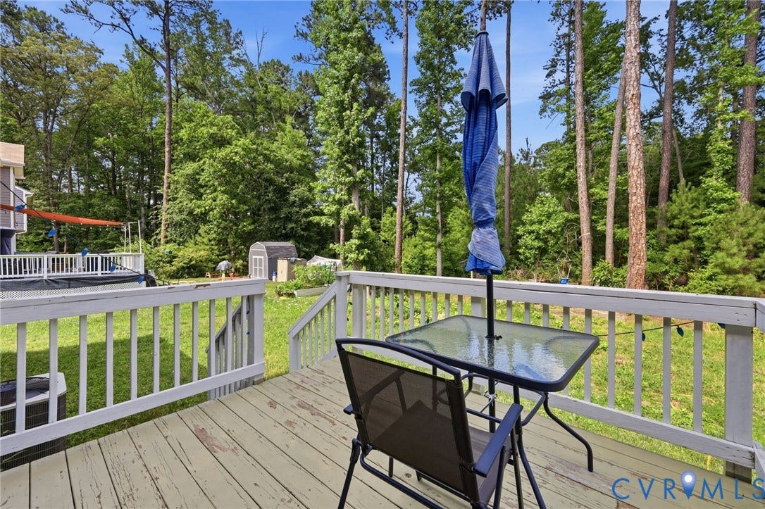 10155 Virginia Road, Glen Allen, VA 23060 Wood-finish deck with white railing, featuring a large grassy yard, mature trees, and a storage shed