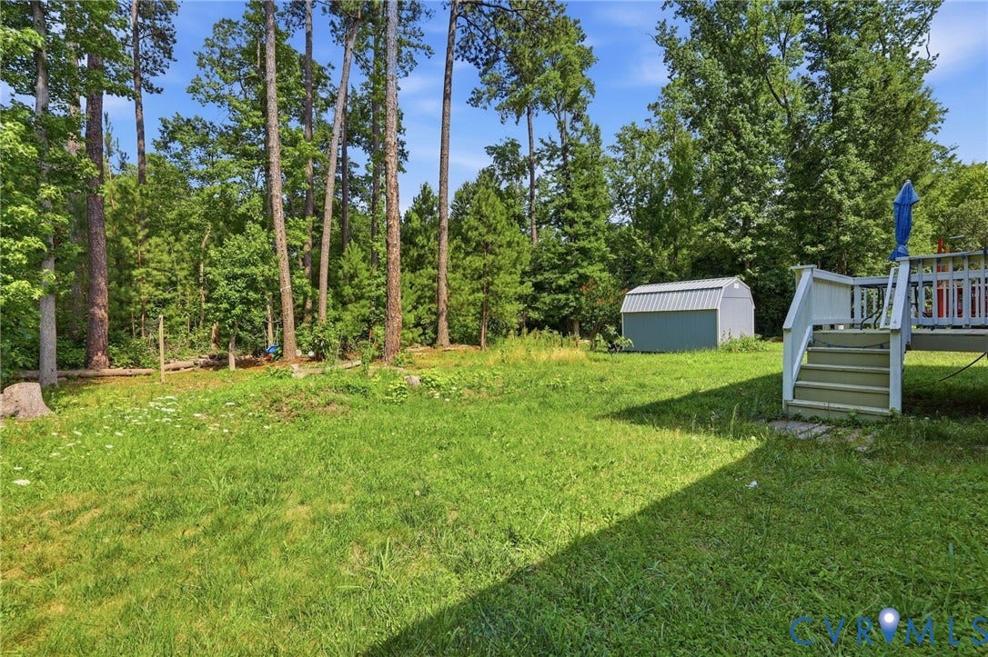 10155 Virginia Road, Glen Allen, VA 23060 Expansive backyard featuring a green lawn, mature trees, a detached storage shed, and a wooden deck with steps