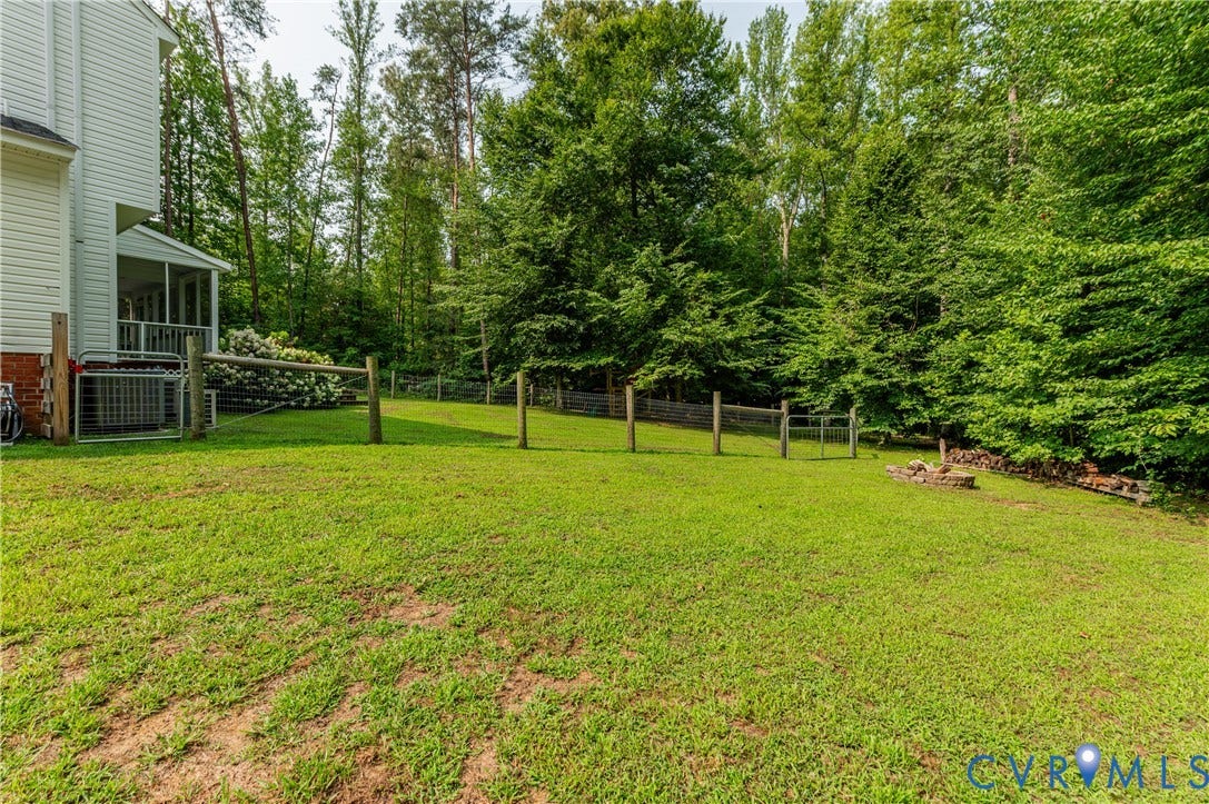 384 Tillar Lane, Mineral, VA 23117 Expansive green lawn featuring a split-rail fence, a stone fire pit, and mature perimeter trees