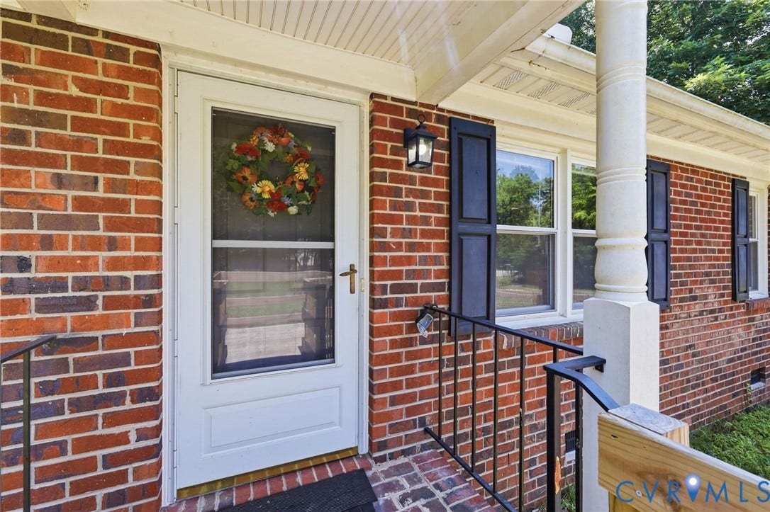 10111 Tunstall Road, New Kent, VA 23124 Brick exterior featuring a white storm door, black louvered shutters, and an exterior wall lantern
