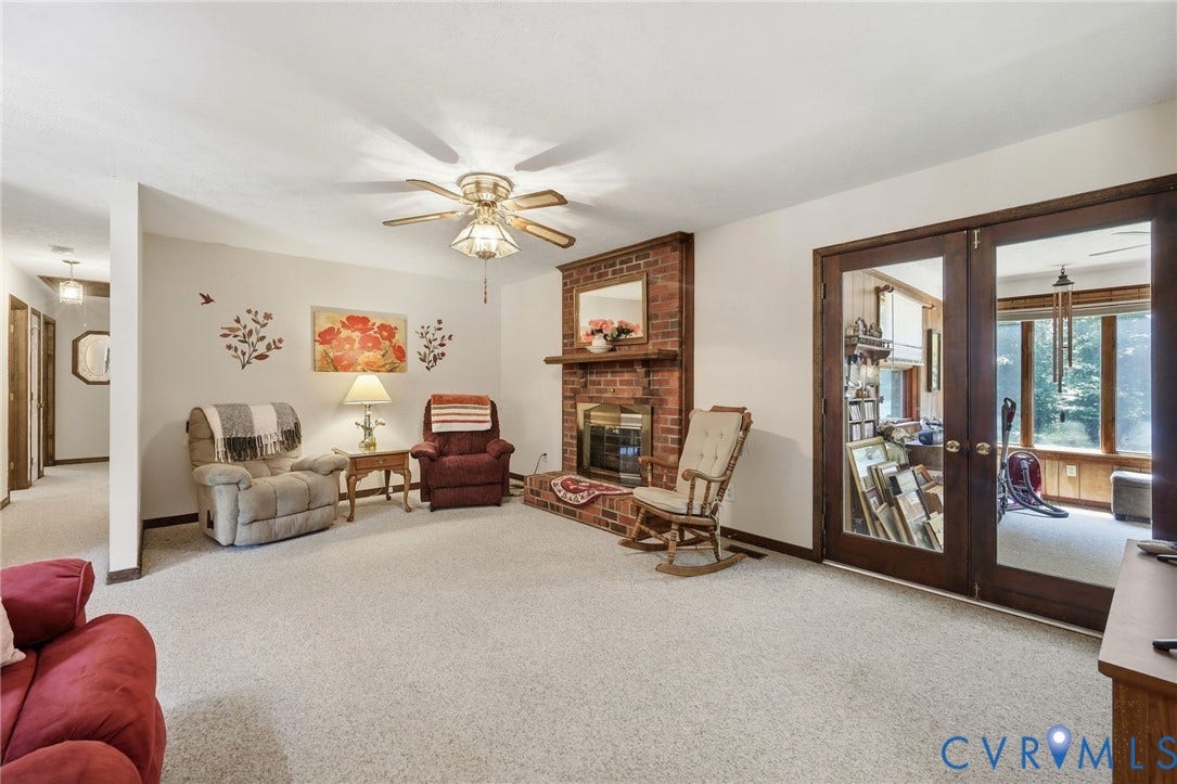 10111 Tunstall Road, New Kent, VA 23124 Living area featuring a brick fireplace with a wood mantle, neutral carpeting, and a ceiling fan with integrated lighting