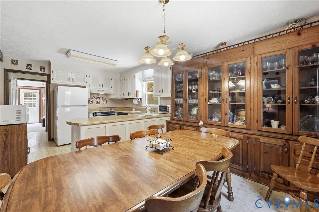 10111 Tunstall Road, New Kent, VA 23124 Spacious eat-in kitchen featuring a large wood-finish dining table, extensive built-in wood-finish cabinetry with glass display doors, white upper and lower cabinetry, white appliances, and a light-colored countertop