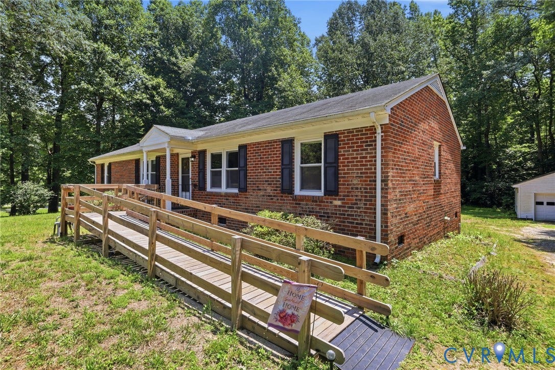 10111 Tunstall Road, New Kent, VA 23124 Brick ranch-style home featuring a covered front entry, accessible ramp, mature trees, and a detached garage structure
