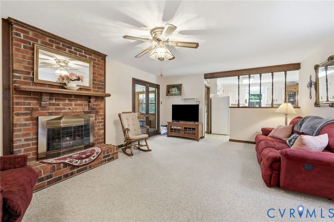 10111 Tunstall Road, New Kent, VA 23124 Living room featuring a brick fireplace with a wood mantle, light-colored carpet flooring, a ceiling fan, and double glass-paneled doors