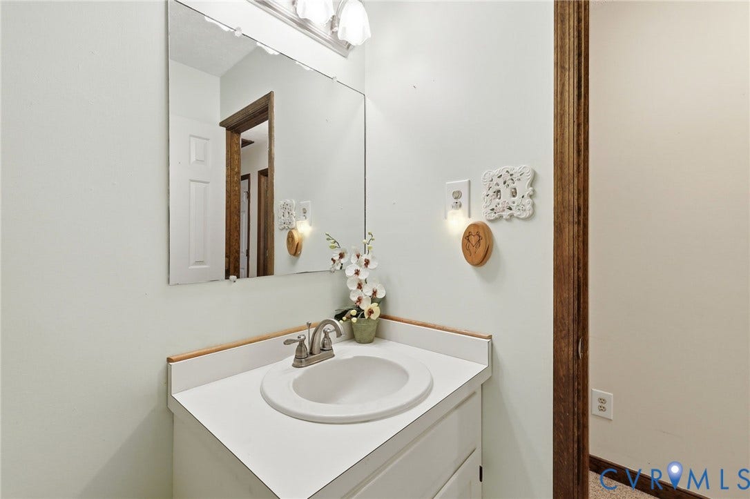 10111 Tunstall Road, New Kent, VA 23124 White vanity with an integrated sink, brushed nickel faucet, large wall-mounted mirror, and overhead vanity lighting