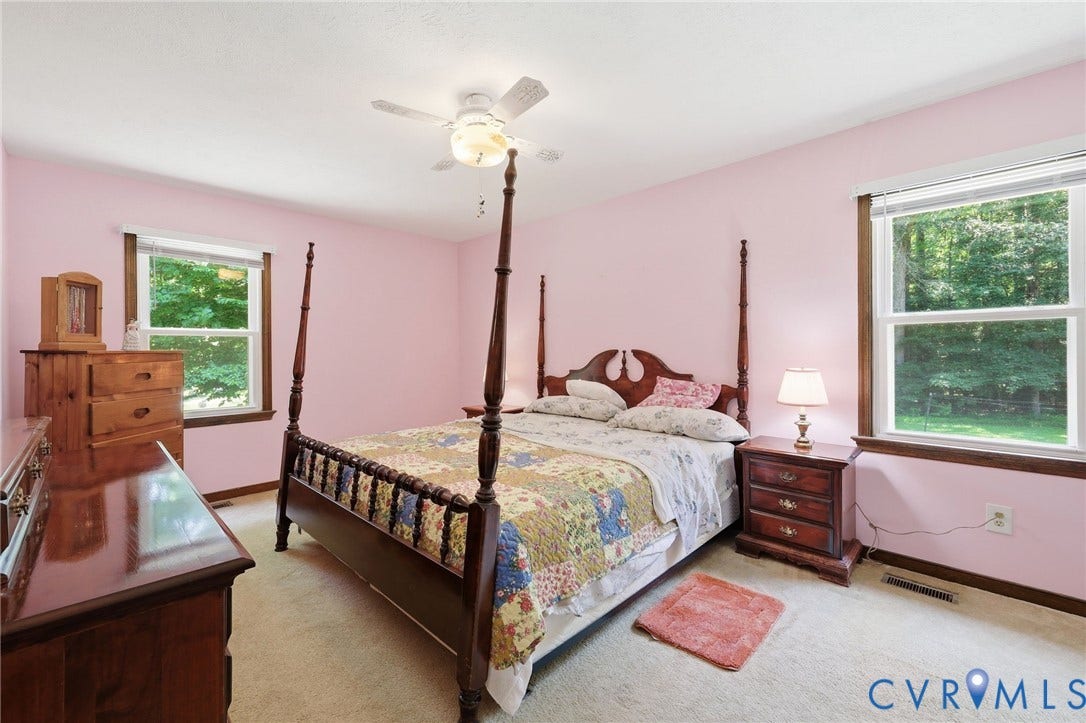 10111 Tunstall Road, New Kent, VA 23124 Carpeted room featuring dual windows with extensive outdoor greenery, a ceiling fan with integrated lighting, and painted walls