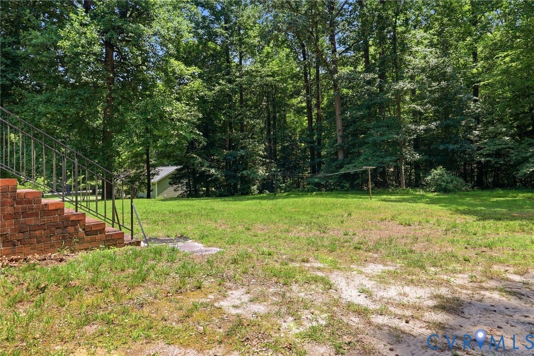 10111 Tunstall Road, New Kent, VA 23124 Expansive rear lawn framed by mature trees, featuring a visible portion of a light-colored structure in the background