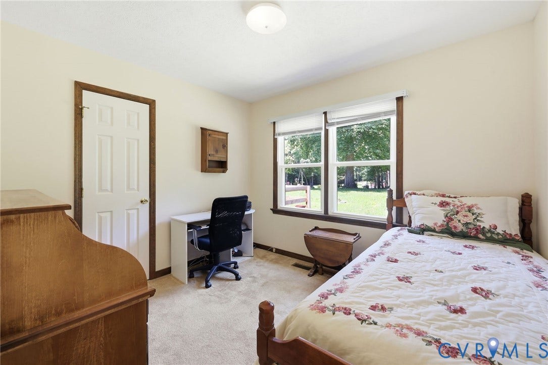 10111 Tunstall Road, New Kent, VA 23124 Carpeted room featuring a white paneled door with wood trim, a built-in wall cabinet, and double windows with wood trim