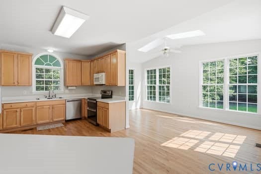 5213 Wheat Ridge Place, Chappell Ridge, Glen Allen, VA 23059 Kitchen and living area featuring wood-finish flooring, a vaulted ceiling with skylights, extensive window placement, light wood cabinetry, and stainless steel appliances