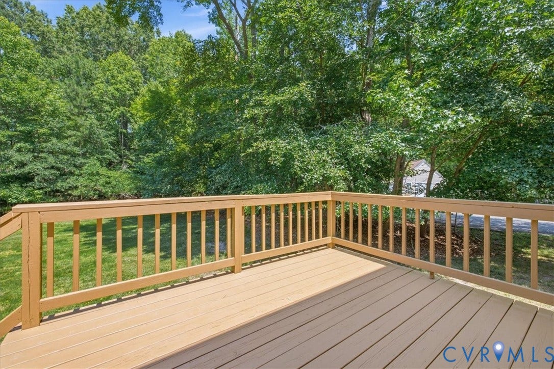 Expansive outdoor deck featuring wood-finish decking and perimeter railings, overlooking a verdant lawn and mature trees