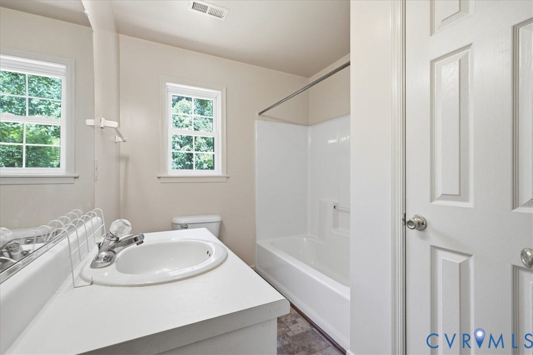 Hall Bathroomupstairs featuring a white vanity with an integrated sink, window with exterior tree scenery, a white toilet, and a white tub with shower surround.  Bonus here is the Linen Closet.