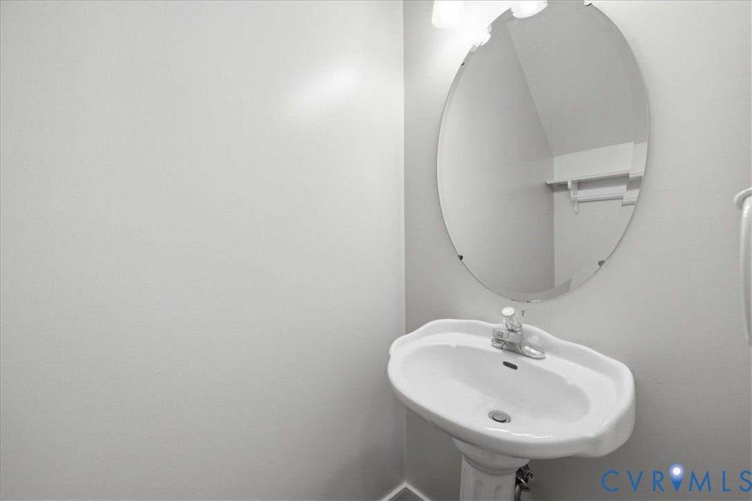 First floor Half Bath features a Pedestal sink with a polished chrome faucet, oval mirror, wall-mounted light fixture, and light-toned wall paint