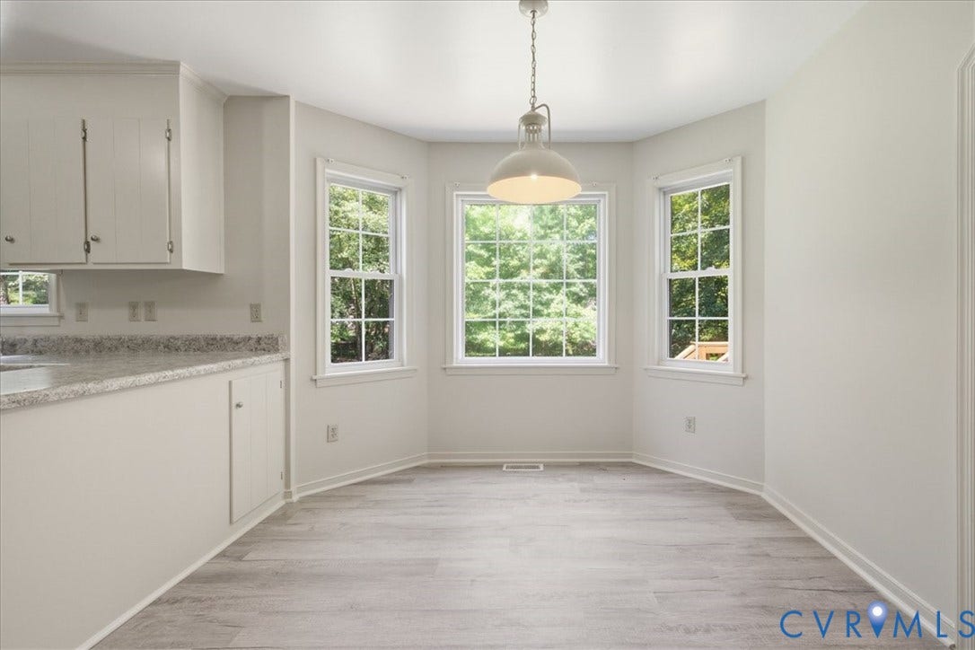 Bay window dining area featuring a pendant light fixture, new flooring, and white cabinetry with a light-toned countertop