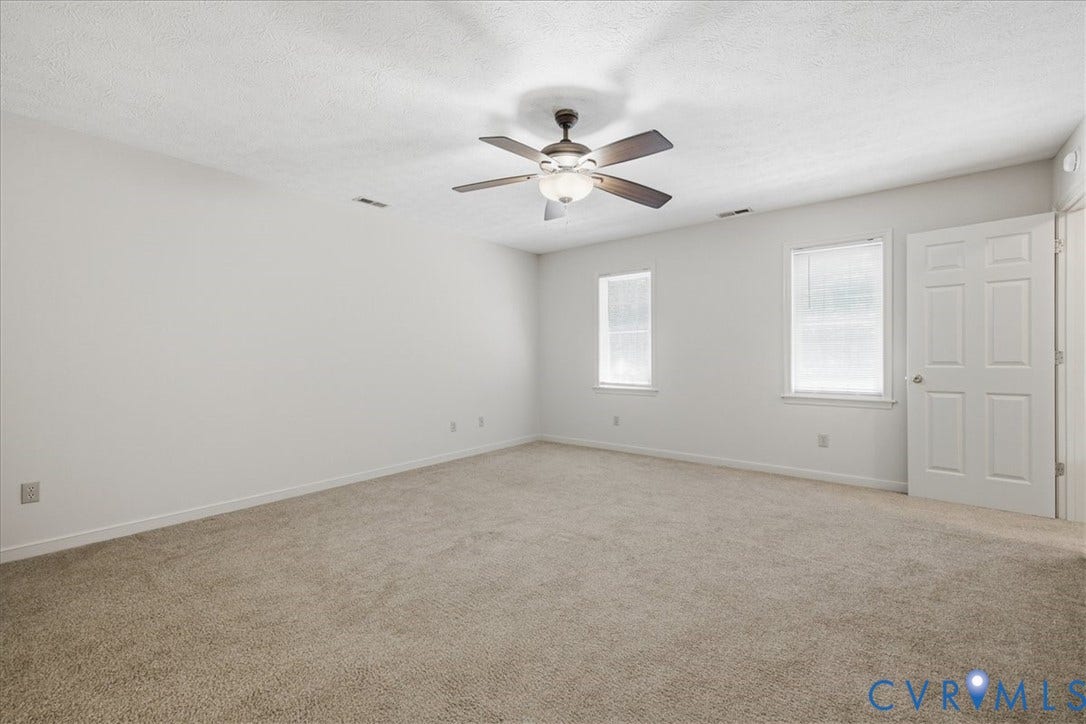 Large, Primary Bedroom has light-colored carpeting, white walls, and a ceiling fan with light fixture