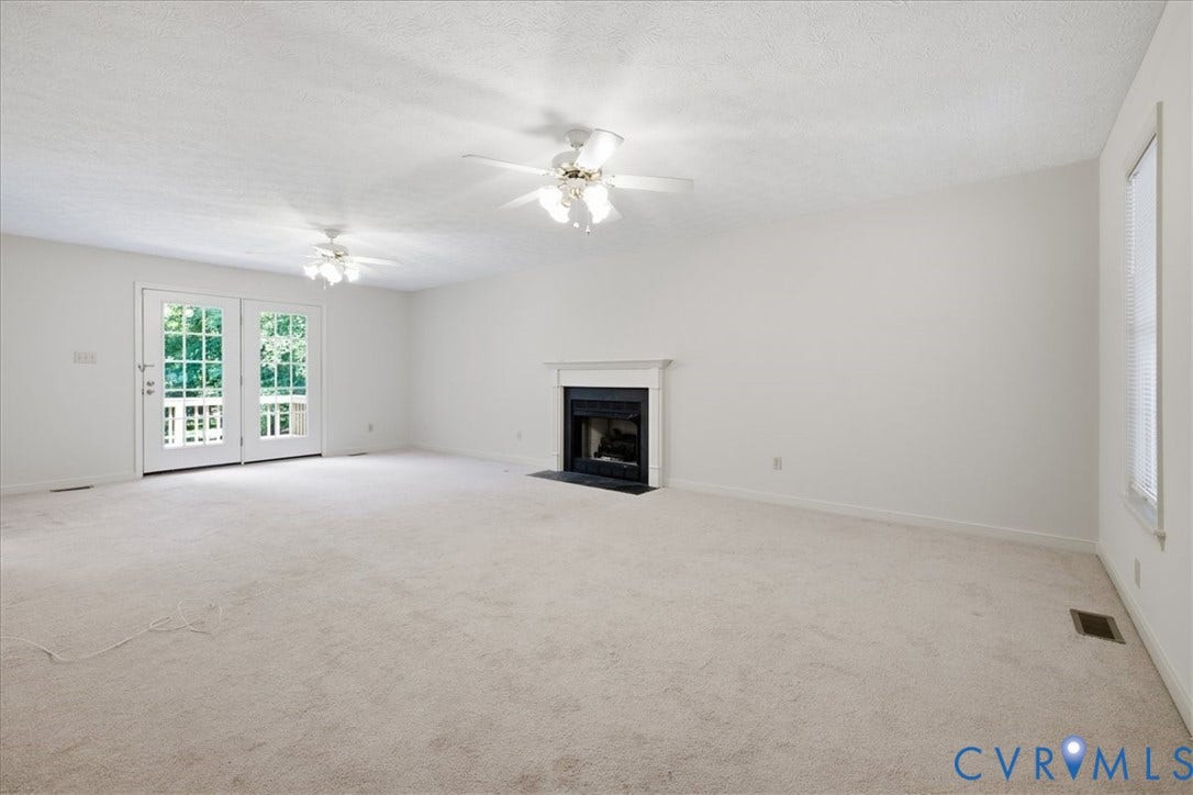 Spacious room featuring light-toned carpeting, a built-in fireplace with a white mantel and dark hearth, and dual ceiling fans