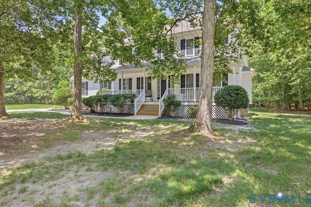 Two-story home with a prominent covered front porch, white railings, and dark louvered shutters