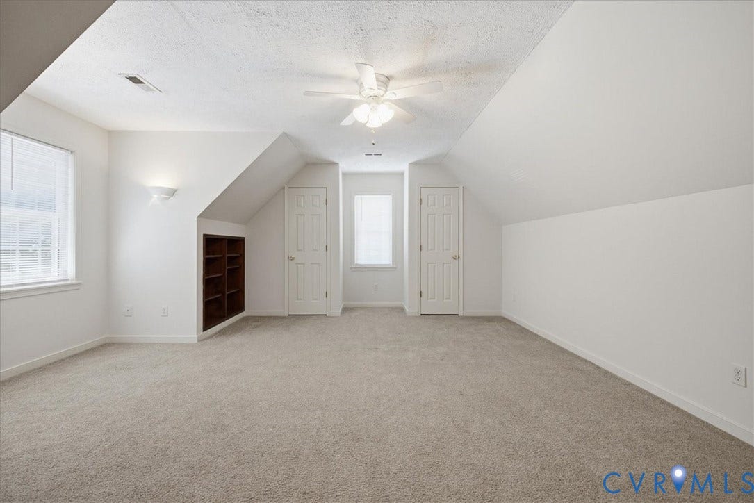 Carpeted bedroom has a ceiling fan, sloped ceilings, and two windows with blinds