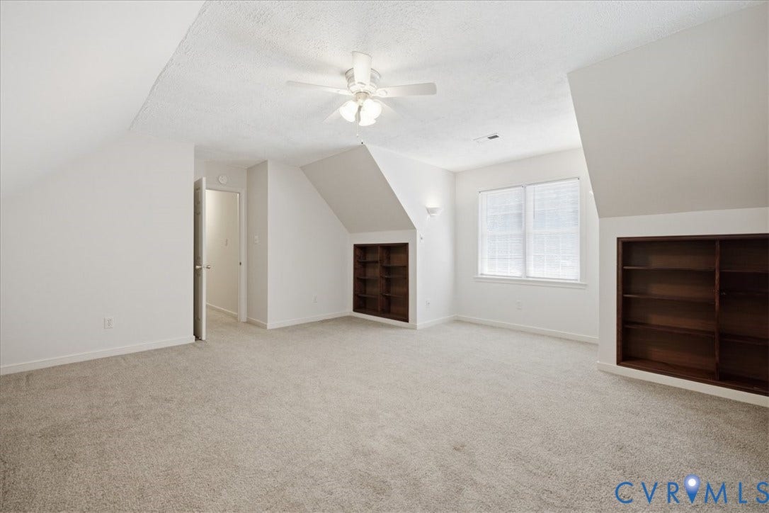 Spacious room featuring sloped ceilings, light-toned carpeting, a ceiling fan, dual built-in shelving units, and two closets.