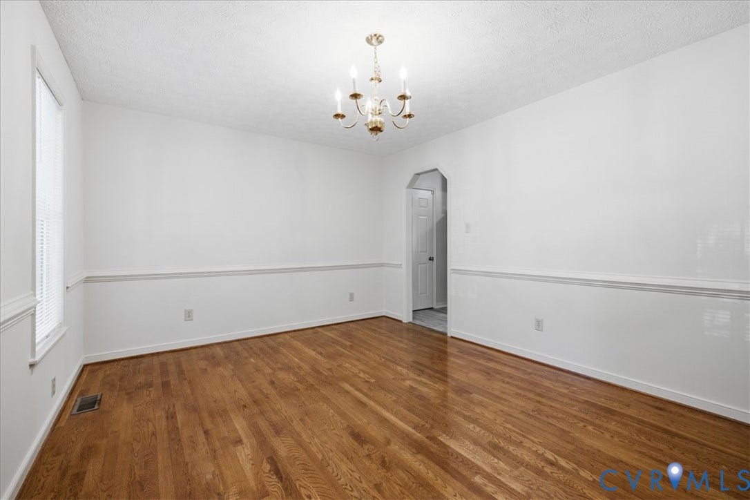 Spacious Dining room featuring wood-finish flooring, a decorative chandelier, white walls with chair rail molding, and a window with blinds