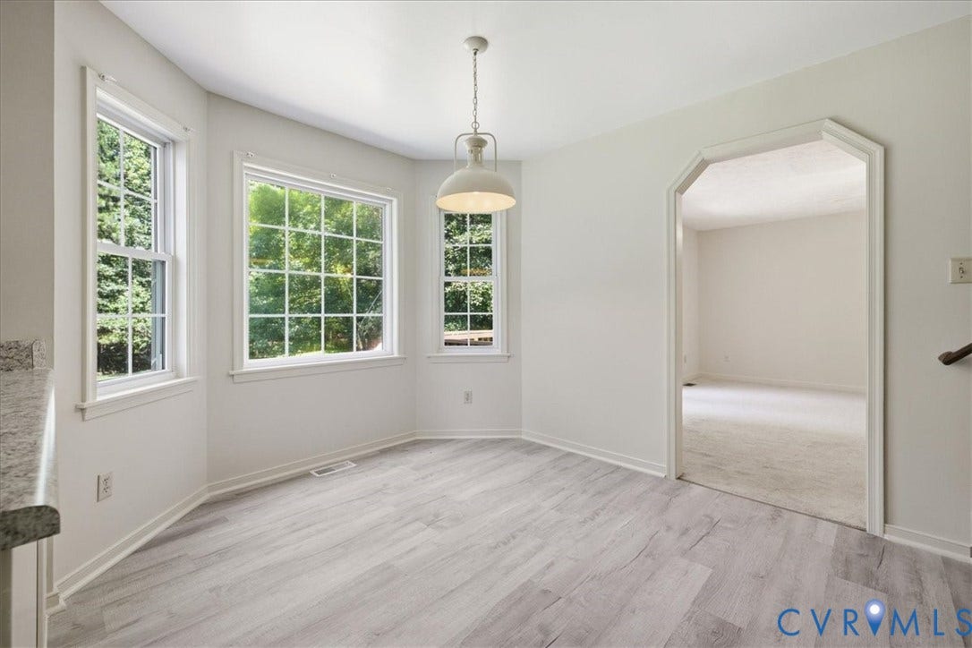 Bay window dining area featuring light new flooring, white trim, and a decorative pendant light fixture