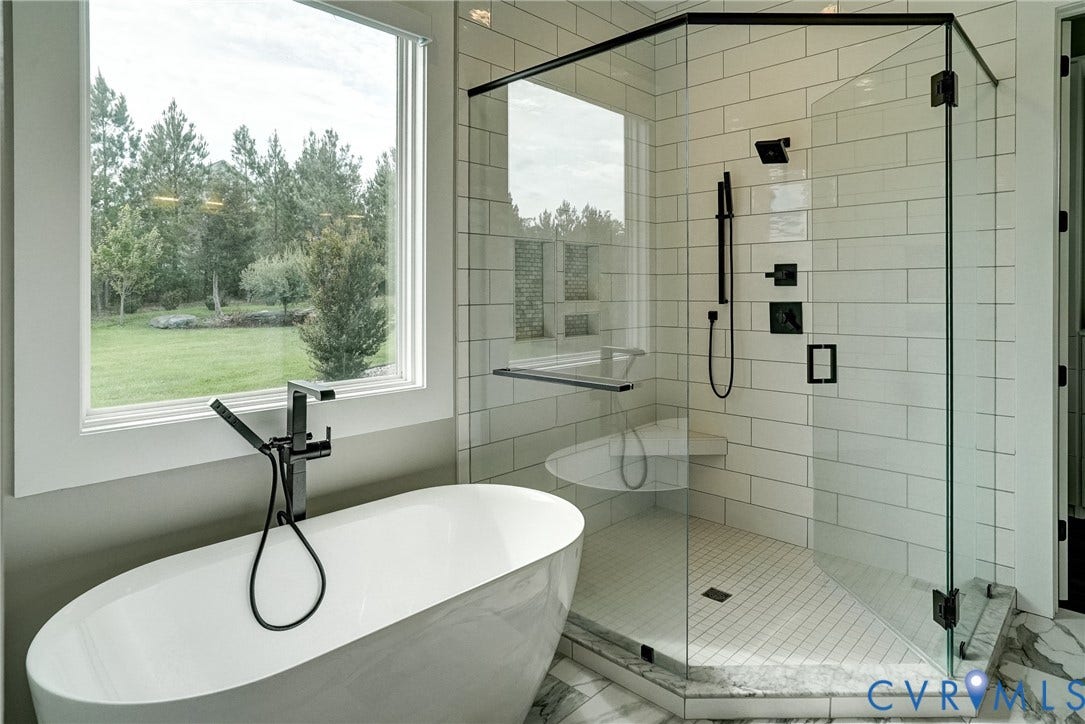 1732 Fishers Pond Drive, Maidens, VA 23102 Freestanding oval soaking tub with a floor-mounted matte black faucet, walk-in shower with matte black fixtures, subway tile surround, and a built-in bench, all set on marble-finish floor tiling