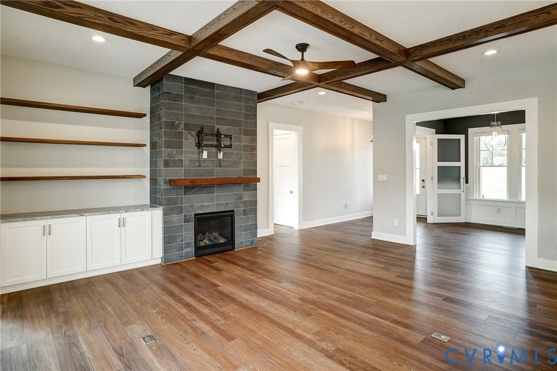 1732 Fishers Pond Drive, Maidens, VA 23102 Open-concept living space featuring wood-finish flooring, a coffered ceiling with exposed wood beams, and a fireplace with a stone tile surround and wood mantel