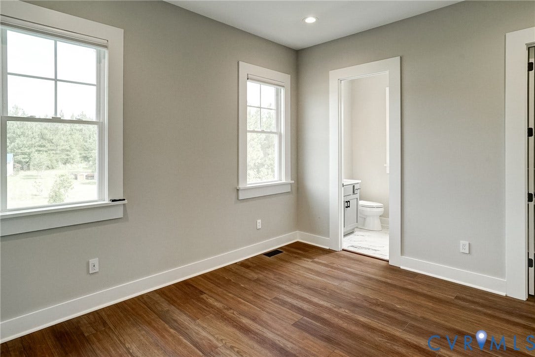 1732 Fishers Pond Drive, Maidens, VA 23102 Spacious room featuring wood-finish flooring, two large windows with white trim, recessed lighting, and a doorway opening to a bathroom with a white vanity and toilet