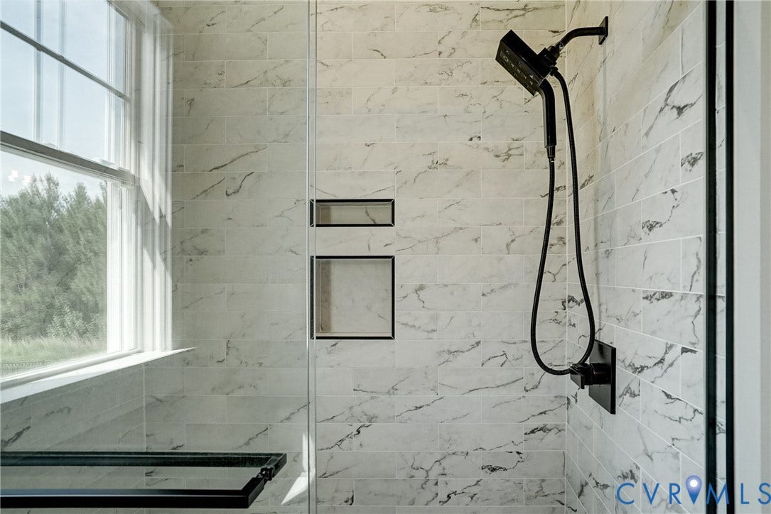 1732 Fishers Pond Drive, Maidens, VA 23102 Shower enclosure featuring subway tile with subtle veining, matte black shower fixtures, two recessed niches, a built-in shower bench, and a large window