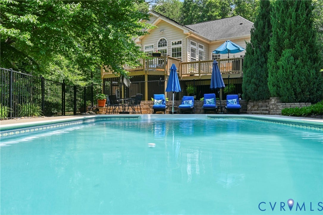 941 Willow Ridge Rd, Zion Crossroads, VA 22974 In-ground swimming pool with a stone retaining wall, bordered by mature evergreen trees and a black iron fence