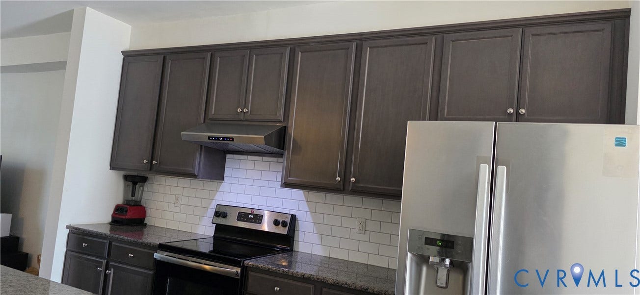 Kitchen featuring dark wood-finish cabinetry, granite-style countertops, subway tile backsplash, and stainless steel appliances including a range and refrigerator