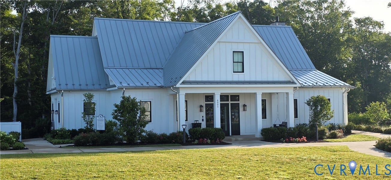 Modern farmhouse exterior featuring white board and batten siding, a metal standing seam roof, a covered entry porch with columns, black-framed windows, and a landscaped front yard