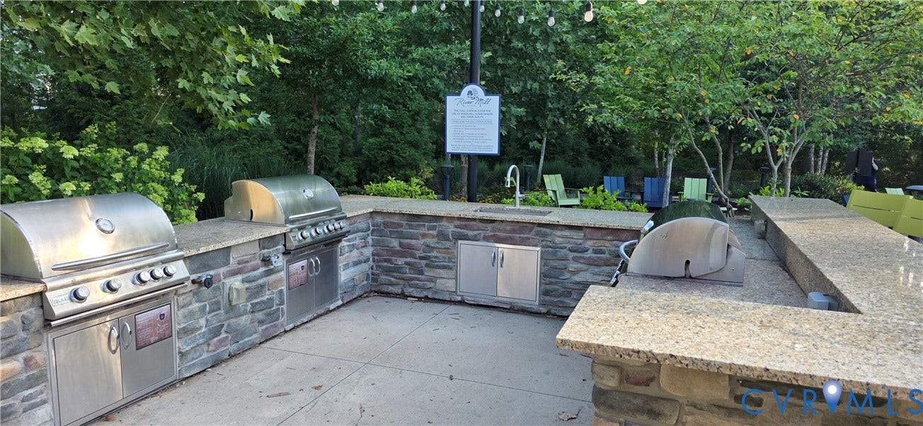 Outdoor kitchen with stone-clad cabinetry, two stainless steel grills, a built-in sink, and extensive countertop space