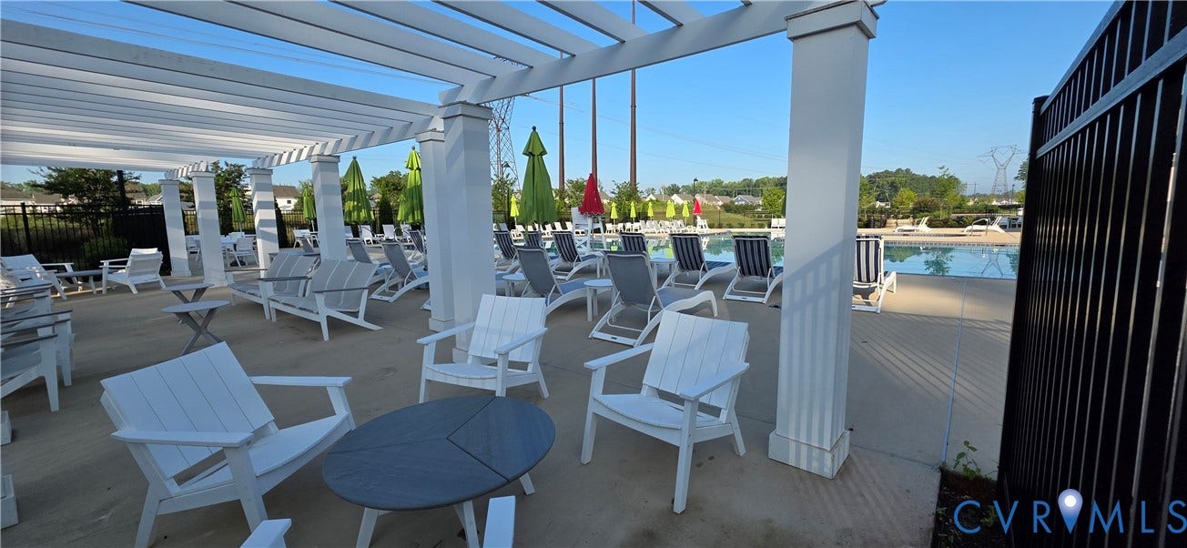 Covered outdoor lounge area featuring multiple white seating arrangements, a pergola structure, a concrete patio, and a black metal fence