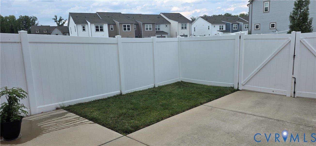 Private outdoor space featuring a white privacy fence, concrete patio, and a grass area